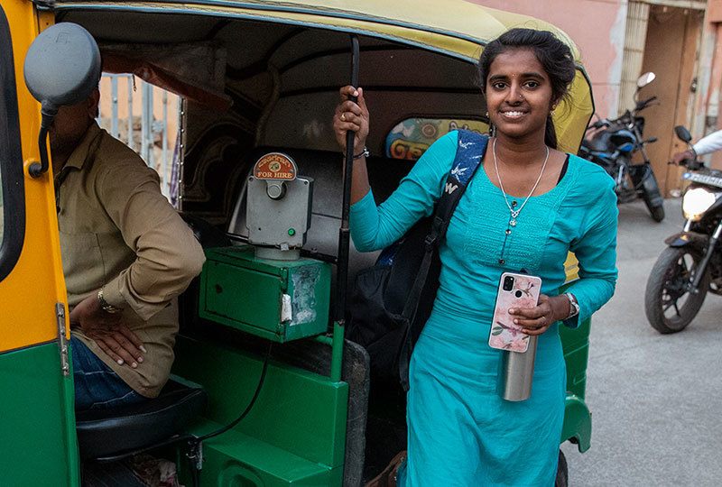 young woman wearing turquoise dress, standing next to cab, smiling at the camera